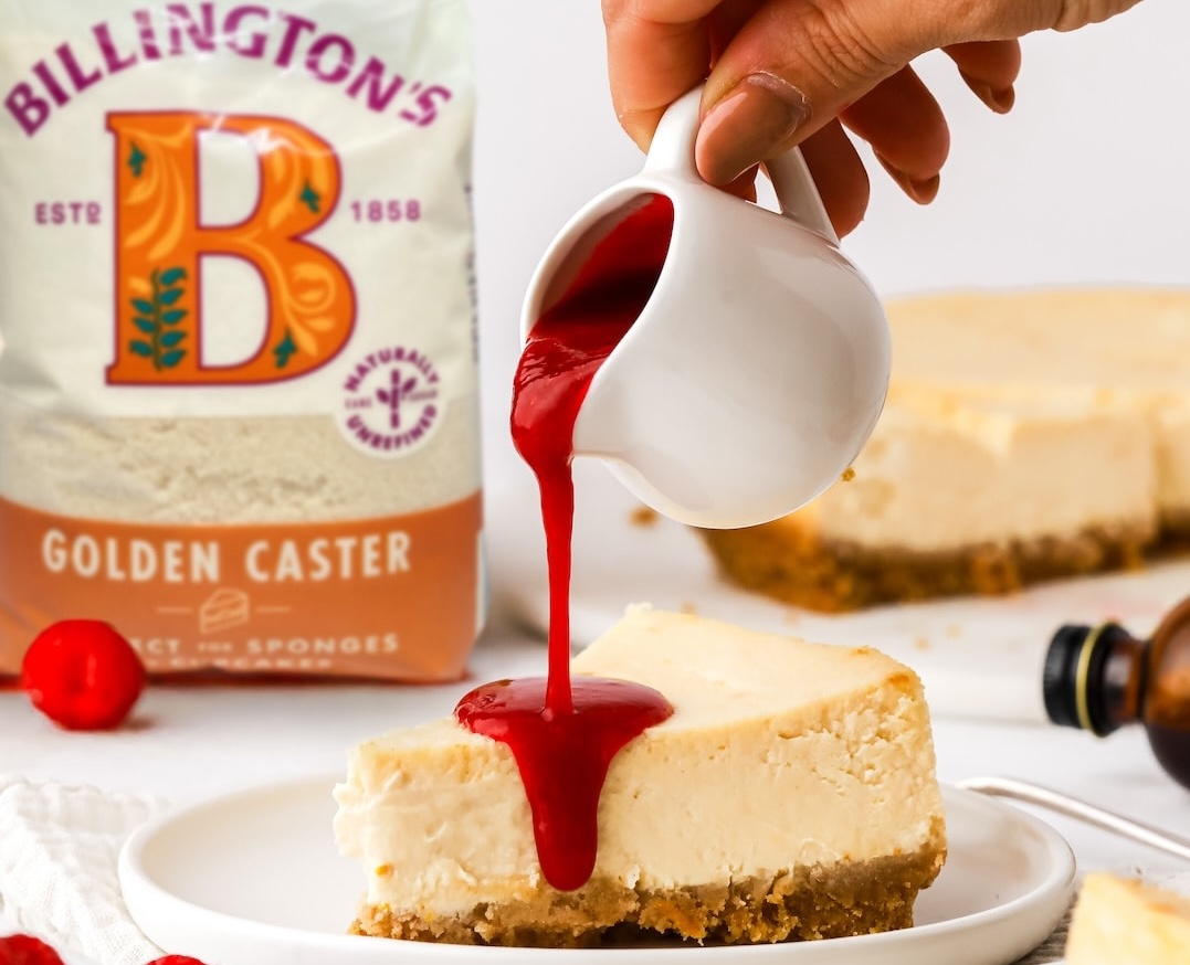A delicious looking baked cheesecake with raspberry coulis, alongside a pack of Billington's Golden Caster sugar.